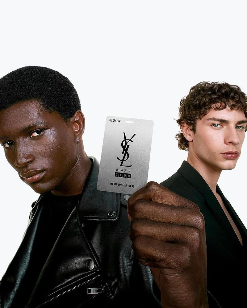 Two men pose with a silver beauty club membership card, showcasing fashion and beauty in a studio setting with clean lighting and modern style.