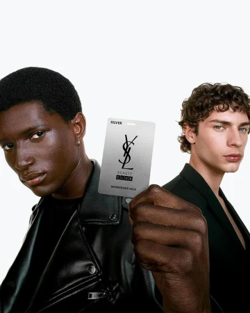 Two men pose with a silver beauty club membership card, showcasing fashion and beauty in a studio setting with clean lighting and modern style.
