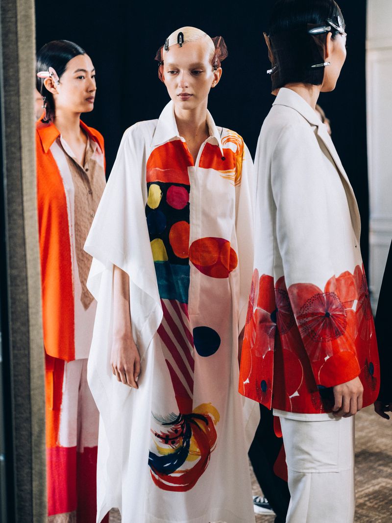 Three fashion models stand side by side wearing brightly colored, patterned clothing in a studio setting during a fashion show.