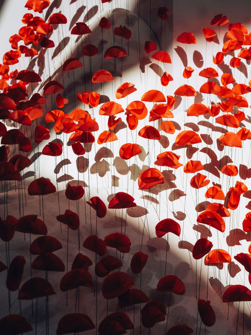 Art installation of red paper flower shapes suspended with string against a white wall, creating a three-dimensional display.