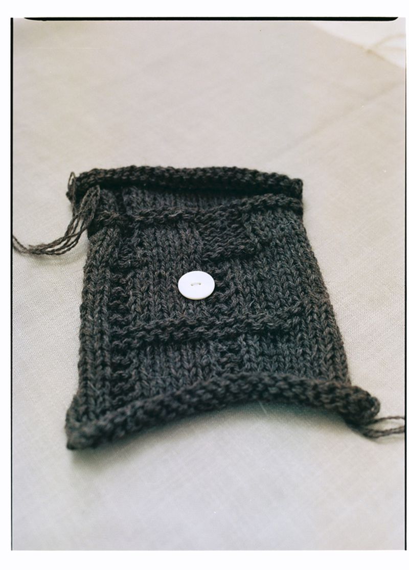 Knitted dark grey bag with a white button closure, showcasing craftsmanship and design on a neutral backdrop.