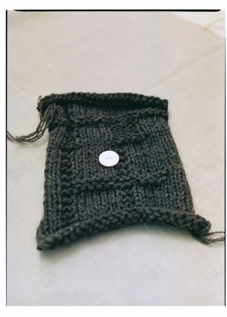 Knitted dark grey bag with a white button closure, showcasing craftsmanship and design on a neutral backdrop.