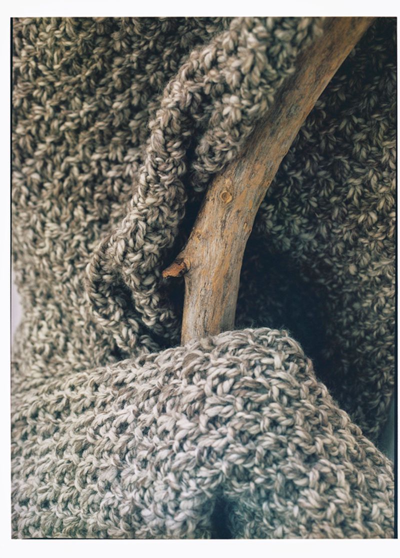 Close-up of a textured grey and beige knitted scarf draped over a natural wood branch, showcasing winter fashion and cozy textures.