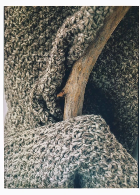 Close-up of a textured grey and beige knitted scarf draped over a natural wood branch, showcasing winter fashion and cozy textures.