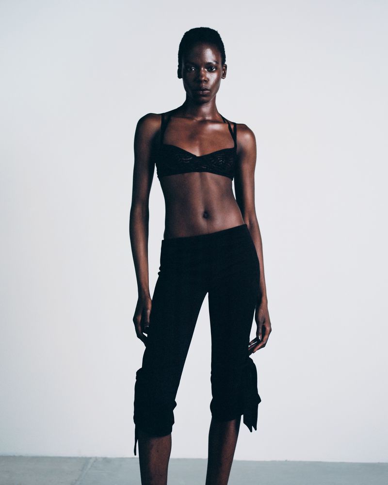 A striking portrait of a fashion model in a bra top and cropped pants against a bright white background, showcasing an editorial style.