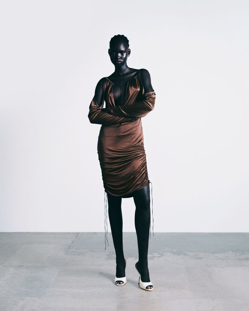 Model wearing a brown satin ruched dress with matching sleeves standing against a plain light background