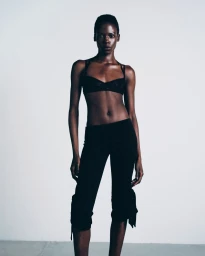 Model standing against a plain white background wearing a black bra and dark trousers from Atlein SS24 collection.