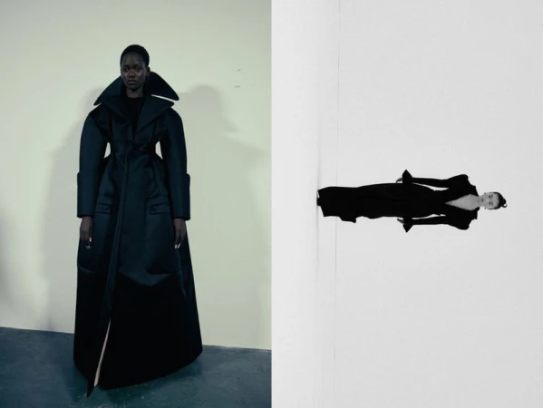 Fashion editorial shot of an African American woman in a black, oversized coat on a cream wall, contrasted with a reversed mirror image.