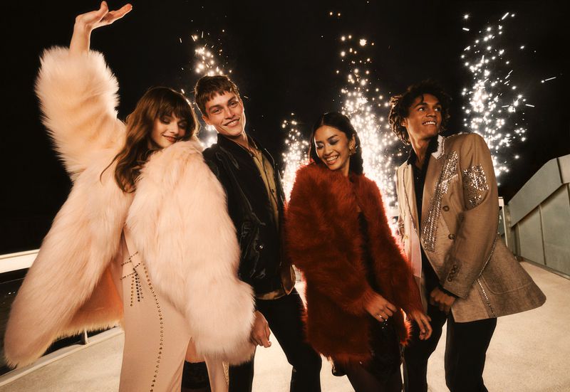 A group of four young adult friends dressed in fashionable outerwear are smiling and laughing in front of a background of firework sparklers.