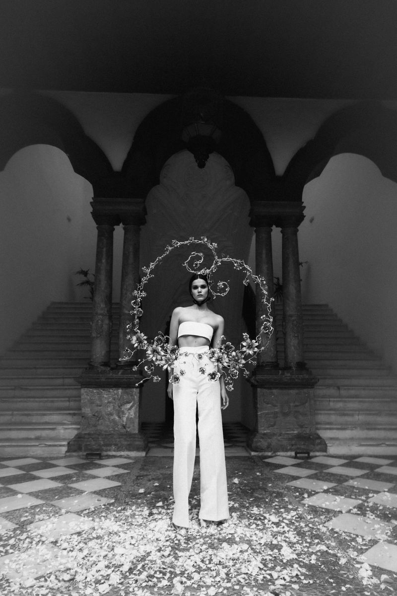 Black and white fashion portrait of a woman in an indoor courtyard with floral accents and a decorative floral frame.
