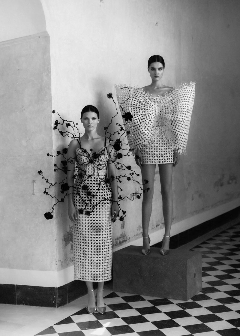Two adult women in architectural fashion, monochrome studio shot, checkered floor, striking design details, and creative presentation.