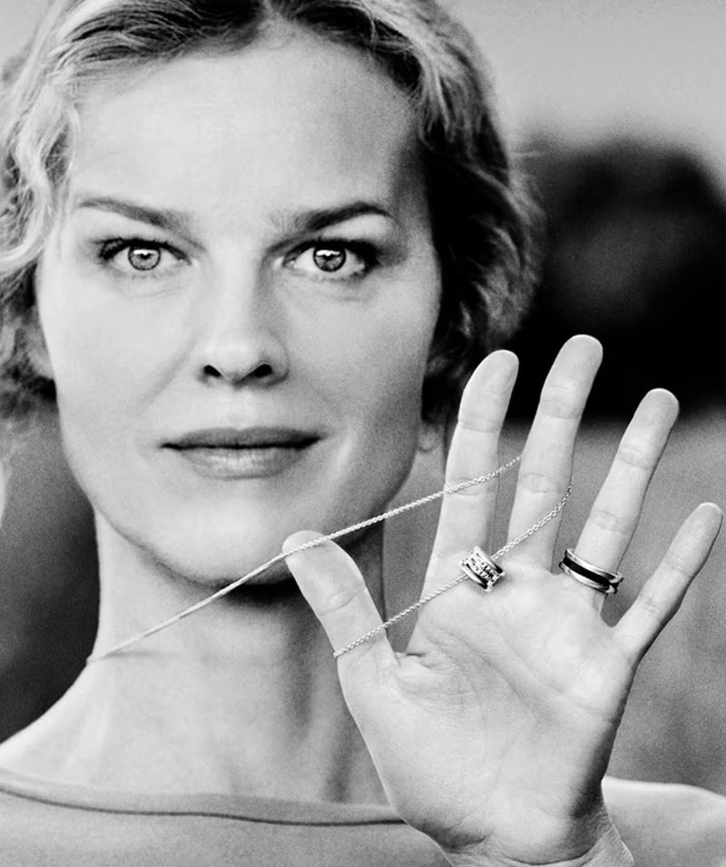 Black and white portrait of a woman holding a necklace and rings, with a soft-focus outdoor background.
