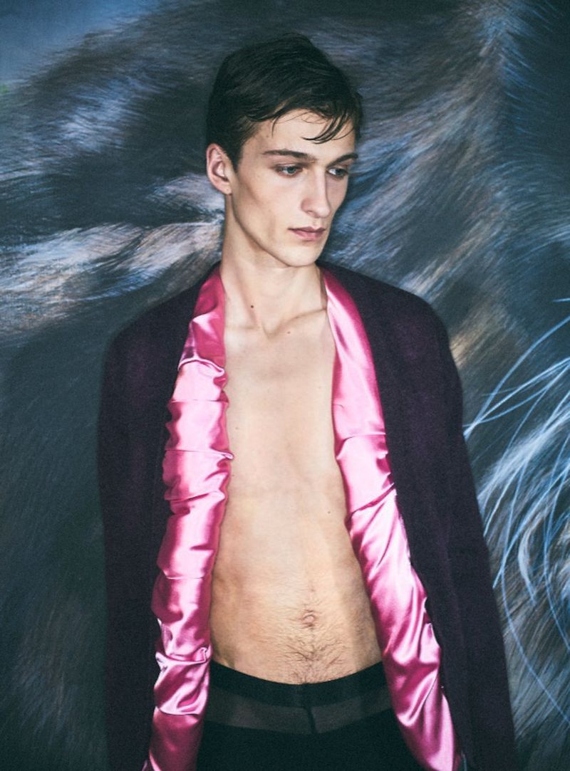 Young male fashion model poses shirtless in front of a tiger print backdrop, showcasing a plum cardigan with pink satin lining.