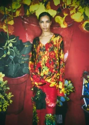 Model wearing a vibrant floral print long-sleeve top and matching skirt against a painted botanical backdrop.