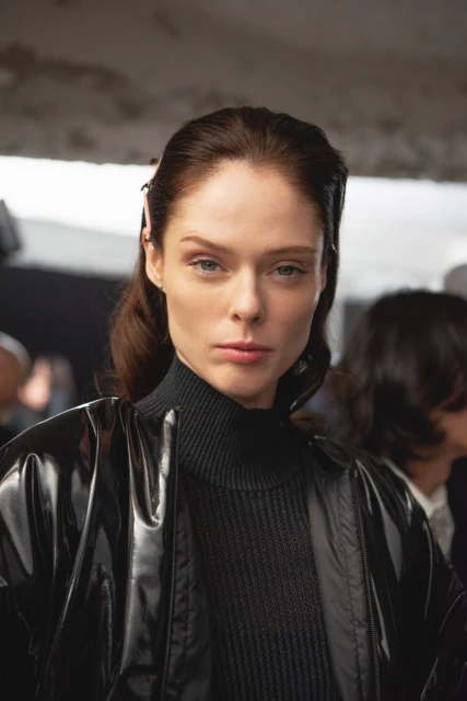 Portrait of a stylish adult woman with auburn hair in a black turtleneck and shiny bomber jacket in a fashion photo studio.
