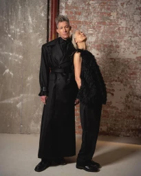 Two models wearing black designer outfits posing against an exposed brick wall background for LGN Louis Gabriel Nouchi.