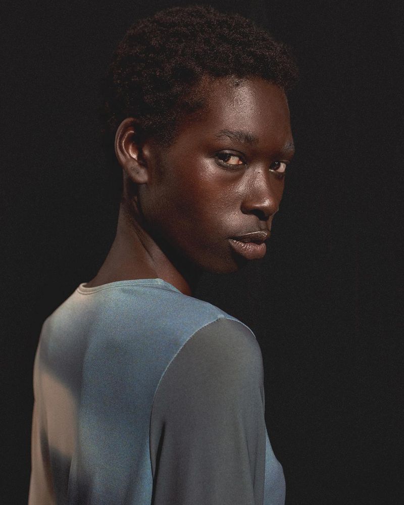 Black model looking back over shoulder wearing a blue and grey top against a dark background