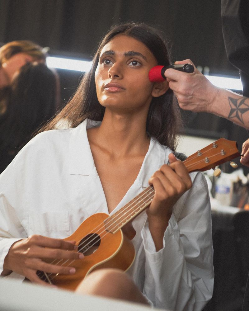 An individual is getting their makeup done while holding a ukulele, focusing on the blend of beauty preparation and musical expression.