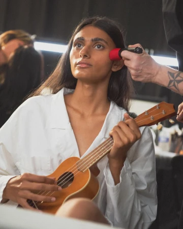 An individual is getting their makeup done while holding a ukulele, focusing on the blend of beauty preparation and musical expression.