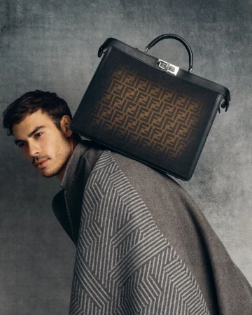 Man poses with Fendi briefcase in a studio setting, wearing a grey patterned coat. Studio portrait capturing high-fashion elegance.