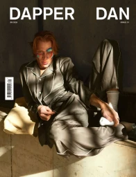 Model with painted face wearing silk pyjamas seated against a textured wall with stark morning light