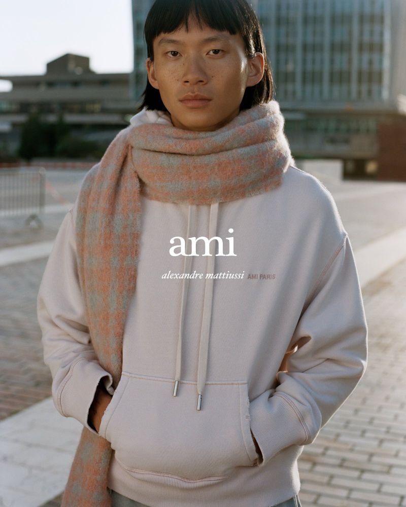 Asian male in outdoor fashion shot wearing a hoodie and scarf in an urban setting with a building in the background.