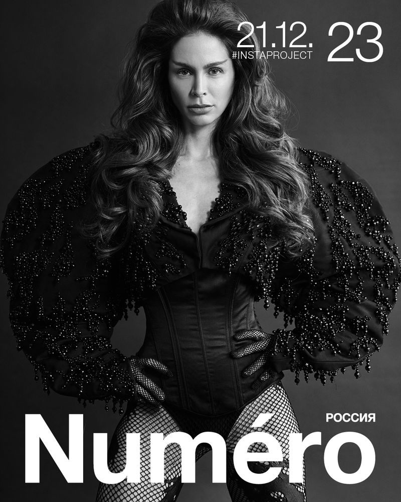 Fashion magazine cover featuring a woman with long, wavy hair, wearing a black embellished jacket, corset, and fishnet stockings, in black and white.