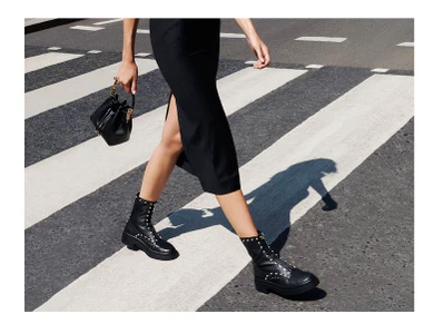 Model walking on a zebra crossing wearing black boots and holding a handbag for Jimmy Choo Fall Winter 2023.