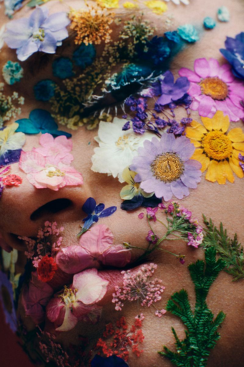 Close-up of a face covered in colorful flowers, creating a vibrant and artistic floral skin effect with pink, purple, yellow, and blue hues.