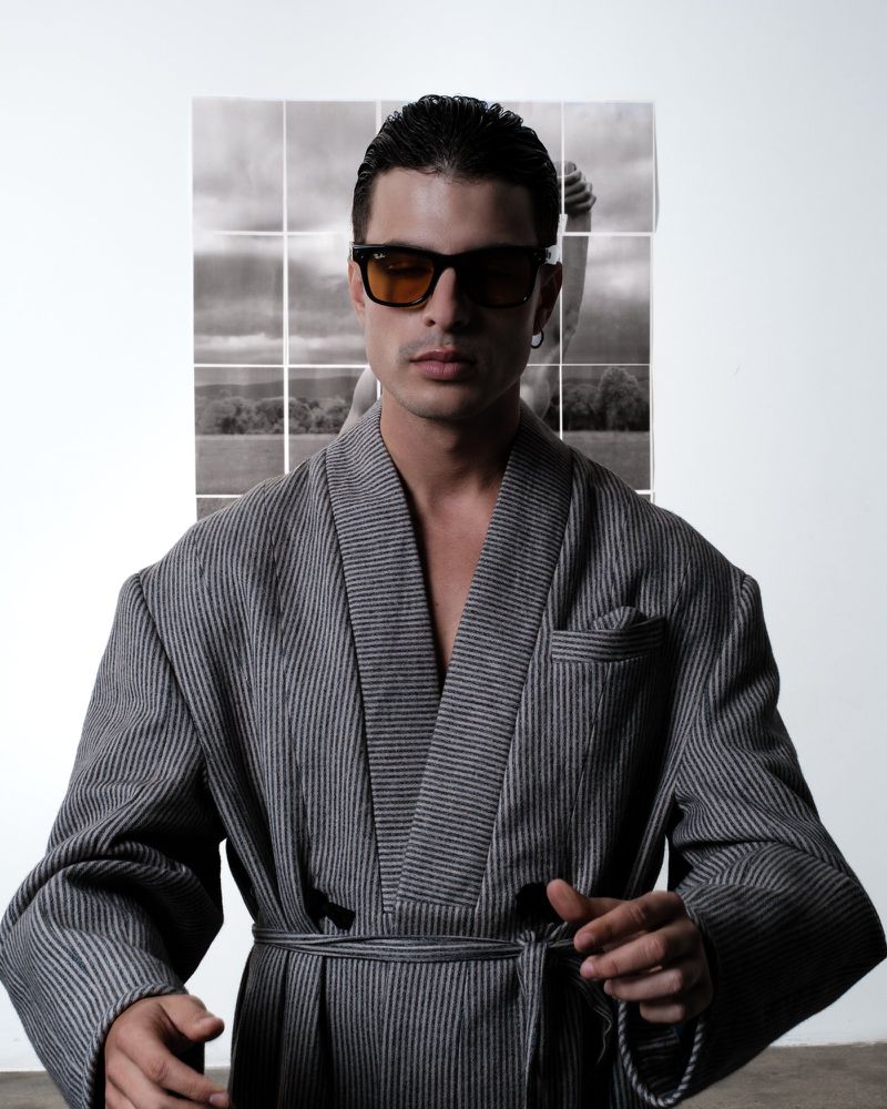 Portrait of a man in a striped robe and sunglasses, posing in front of a nine-panel black and white landscape photo.
