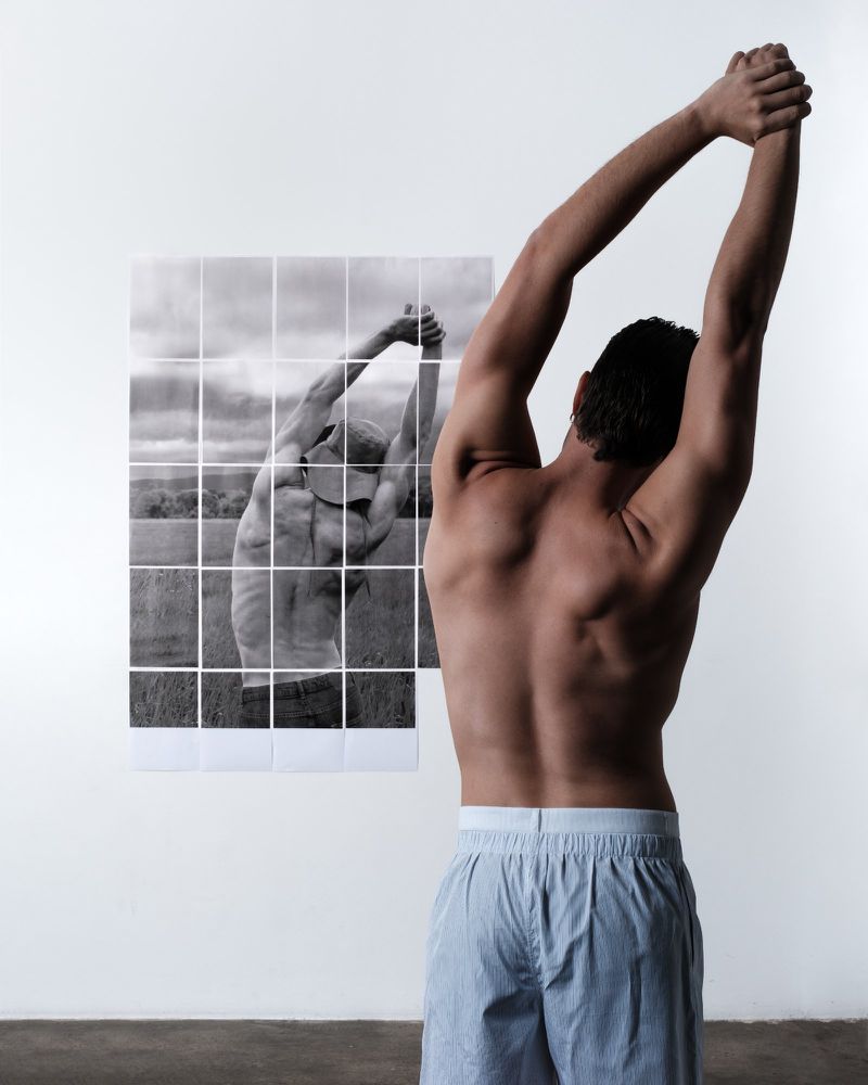 Rear view of a shirtless man stretching with arms raised near a gridded black and white photo of a man in the same pose.