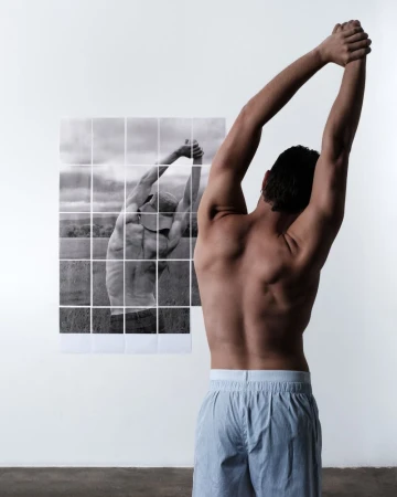 Rear view of a shirtless man stretching with arms raised near a gridded black and white photo of a man in the same pose.