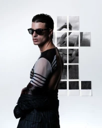 Man wearing dark sunglasses and a sheer striped top looking over his shoulder against a plain white background with a collage of photographs