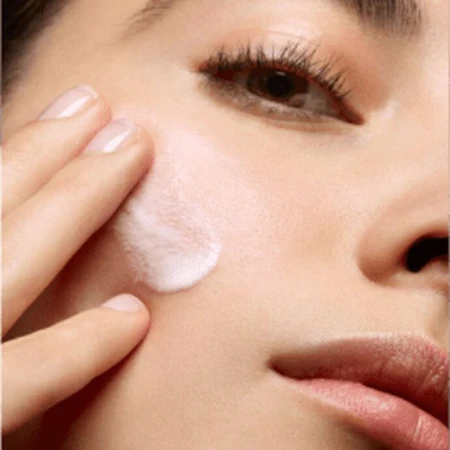 Close-up of an adult female applying cream to her face with her fingers, showcasing skincare and beauty with focus on health.