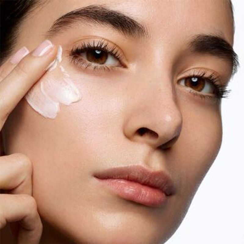 Close-up of an adult woman applying white cream to her face with her fingers, highlighting her skincare routine against a clean background.
