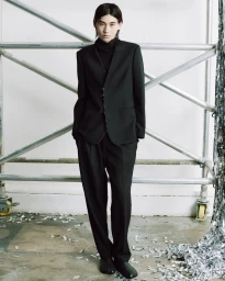 Model in a black suit and turtleneck standing against scaffolding for MM6 Maison Margiela