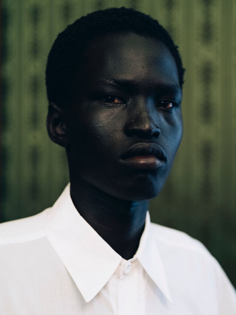 Portrait of a Black male model wearing a white collared shirt against a patterned green background.