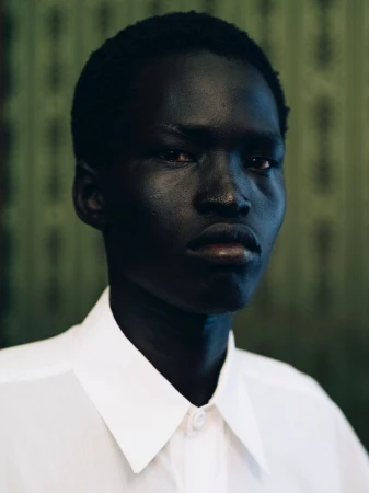 Portrait of a Black male model wearing a white collared shirt against a patterned green background.