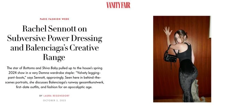 Woman in black top and velvet skirt with a black purse, leaning against a wooden wall; fashion editorial in an indoor setting.