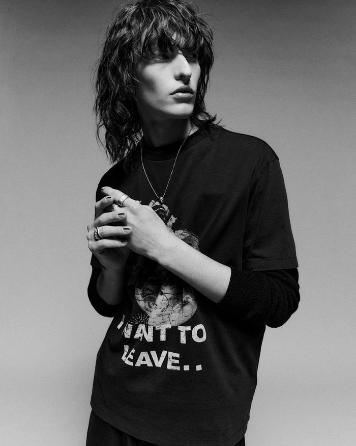 Monochrome portrait of a male model in a black graphic t-shirt holding his hands together against a gradient studio background.