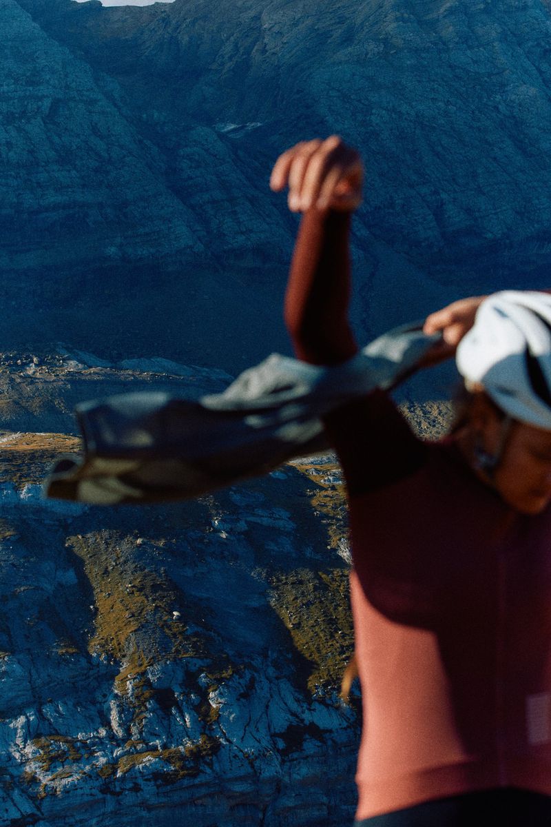 Female cyclist in cycling helmet and apparel holds jacket on rocky mountain landscape. Sporty woman in outdoor cycling setting.