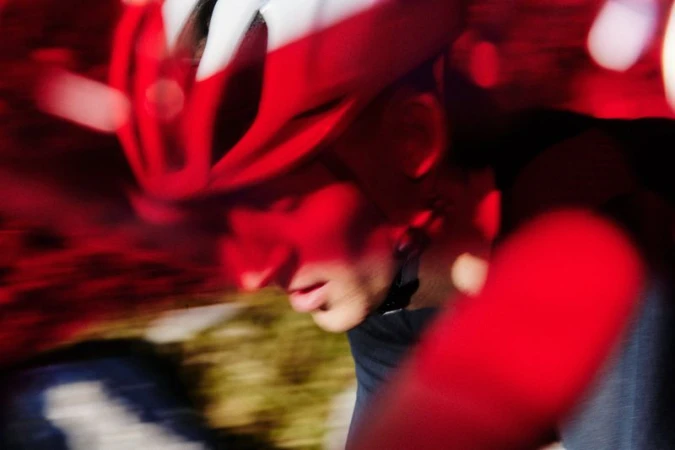 Close-up action shot of a cyclist wearing a red helmet and dark jersey, captured with motion blur during a ride.