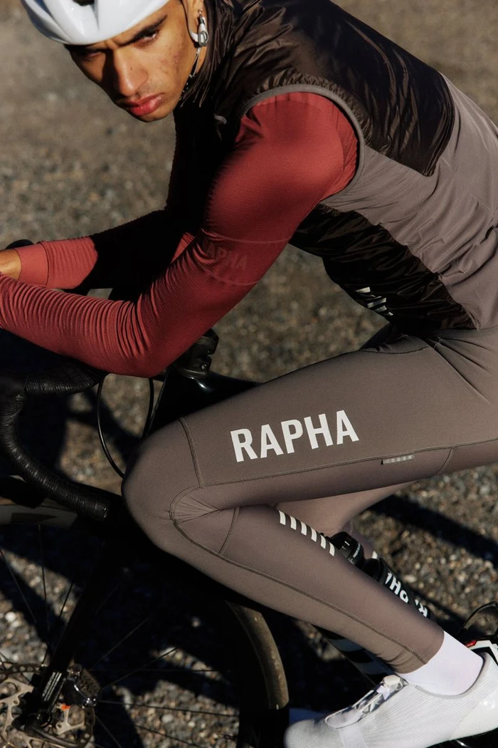 Cyclist in brown cycling jersey and bib shorts leaning over a road bicycle outdoors