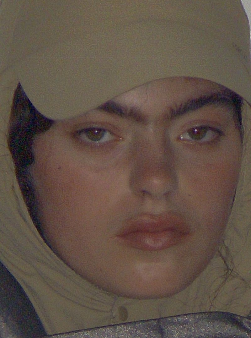 Close-up portrait of a young adult female with brown hair and eyes, wearing a tan hood, shot with eye-level angle and natural light.