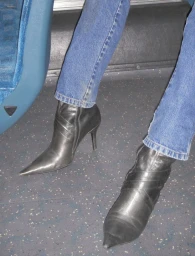 Close-up of legs in blue denim jeans and pointed-toe black leather stiletto ankle boots on a transit bus floor.