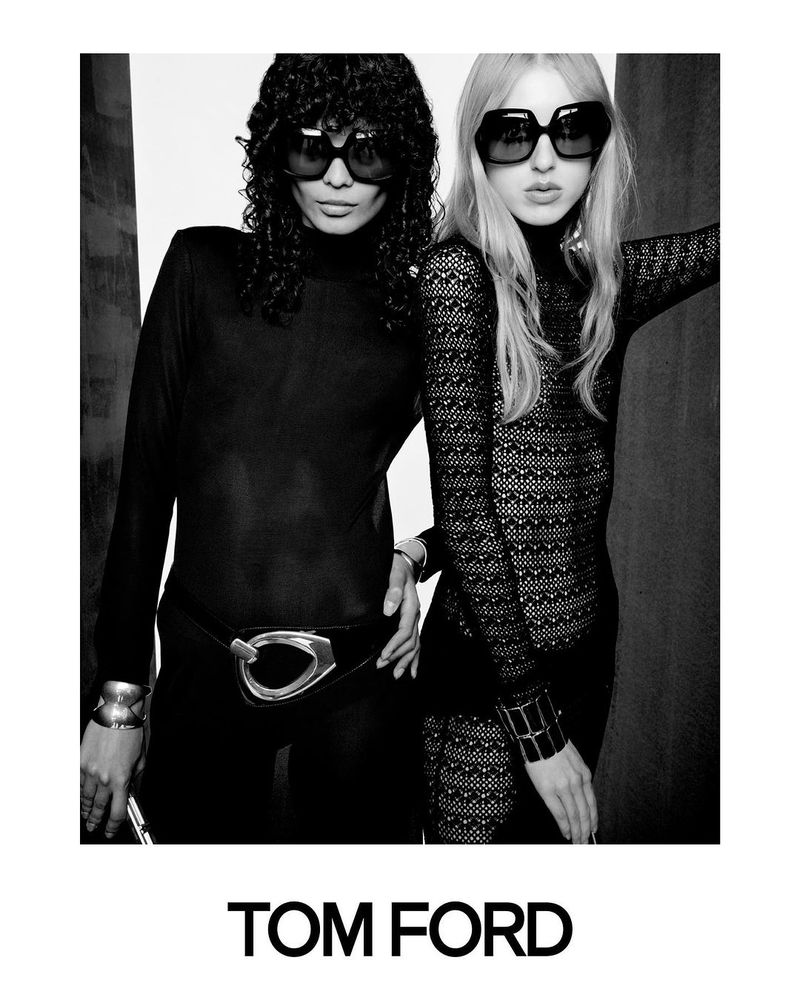 A black-and-white fashion shot features two women in dark tops and sunglasses, standing close to each other, showcasing a stylish, monochrome aesthetic.