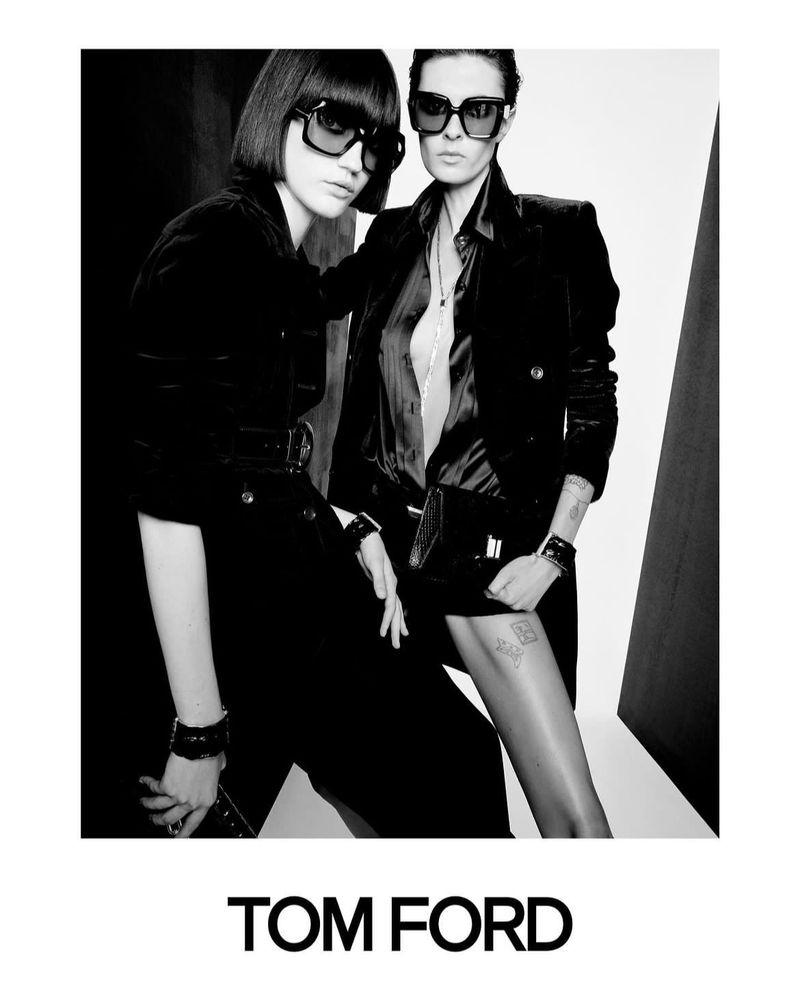Black and white fashion shot of two women modeling sunglasses and black velvet jackets in a studio setting for a Tom Ford advertisement.