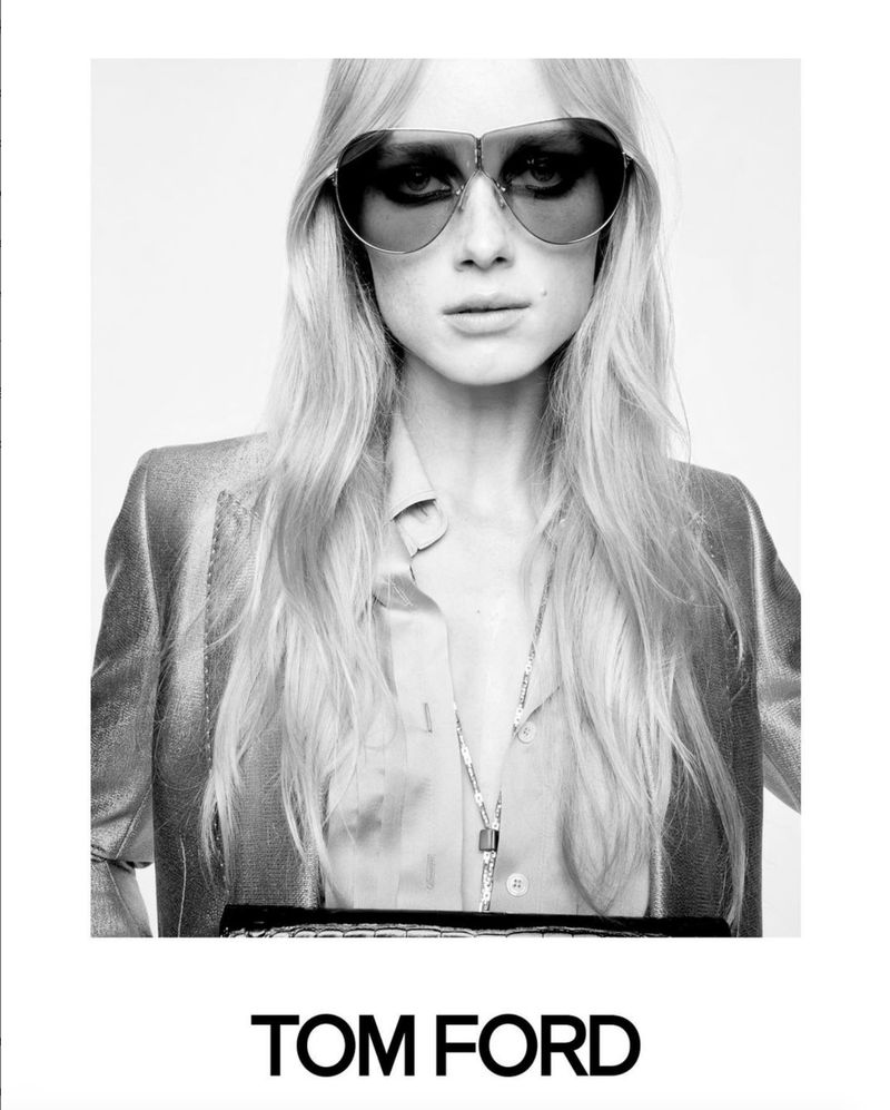 Black and white portrait of a fair-skinned woman with long blonde hair, wearing oversized sunglasses and a shiny jacket, Tom Ford logo.