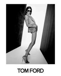 Model wearing oversized dark sunglasses, a tailored tweed blazer, and high-heel sandals in a black-and-white studio setting for Tom Ford.