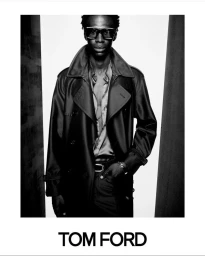 A Black male model wearing dark oversized sunglasses, an unbuttoned shirt, and a belted trench coat for a Tom Ford campaign.